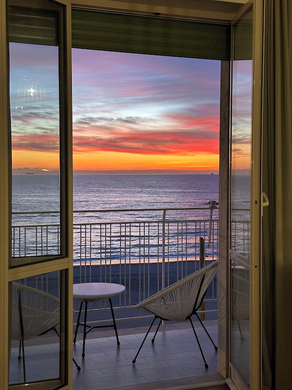 Un balcón con vista al océano al atardecer, dos sillas y una mesa.