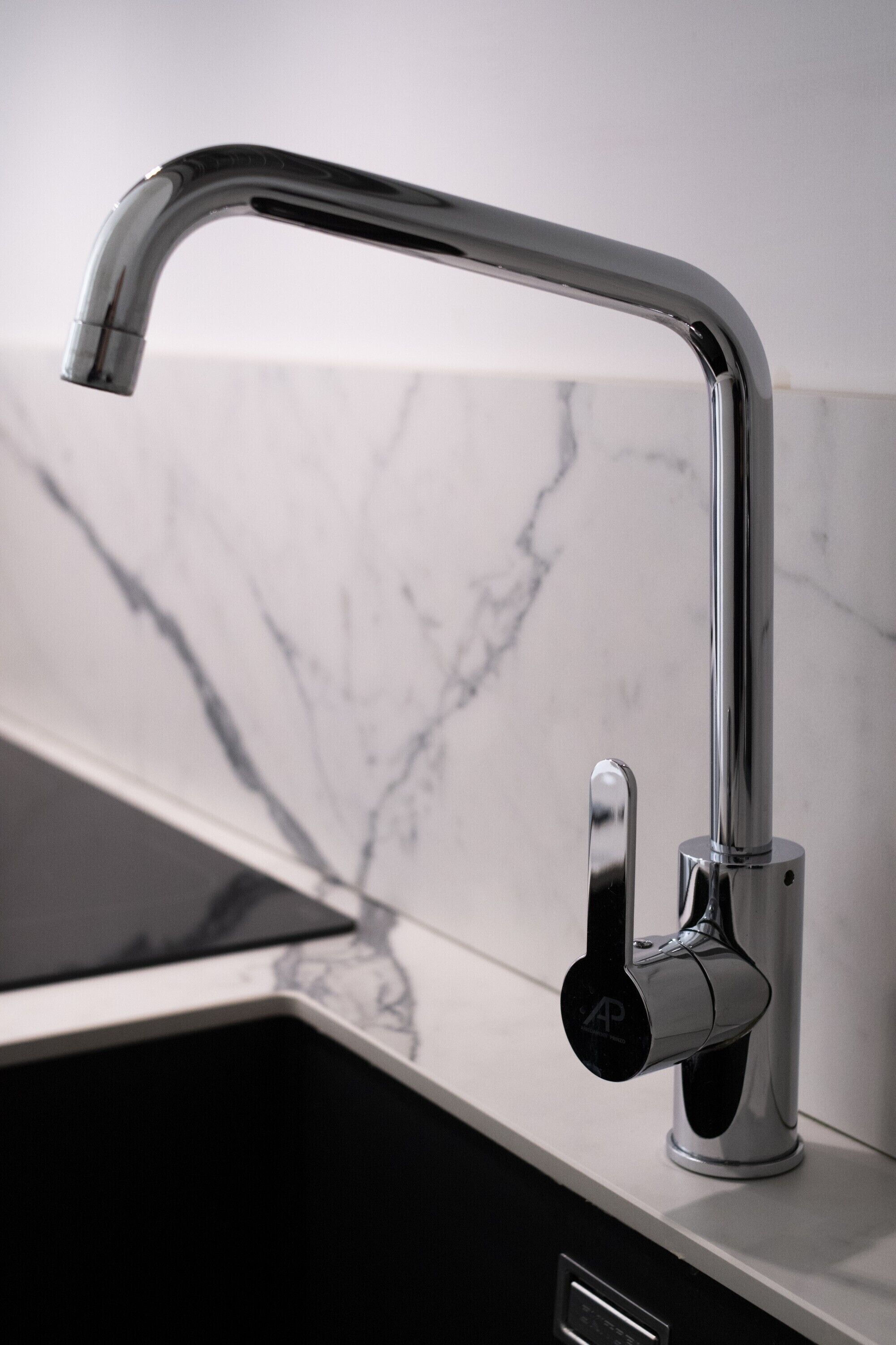 A modern kitchen with a sleek faucet, a marble backsplash, and a black countertop.