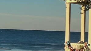 Ein weißes Kiosk mit einem dekorativen Kranz, mit Blick auf einen Strand und ruhige Wellen.