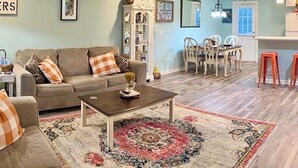 Ein Wohnzimmer mit einer Couch, einem Couchtisch und einem Teppich. Es gibt eine Essecke mit Stühlen und einem Tisch.