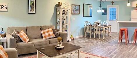 A living room with a sofa, coffee table, and a rug. There is a dining area with chairs and a table.