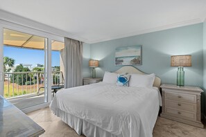 Une chambre avec un grand lit, deux tables de chevet avec des lampes, un tableau au mur et une vue sur l’extérieur, accessible par une porte-fenêtre coulissante.
