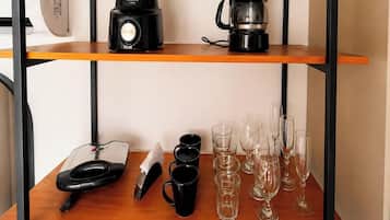 Una encimera de cocina con una cafetera, una balanza, tazas y copas de vino.