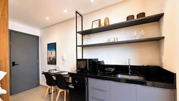 A modern kitchen with black countertops, a refrigerator, a microwave, and a sink. There are two black chairs and a dining table.