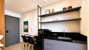 Une cuisine moderne avec des plans de travail noirs, un réfrigérateur, un four à micro-ondes et un évier. On y trouve deux chaises noires et une table à manger.