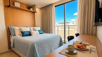 Una habitación de hotel con cama, una mesa de comedor con desayuno y un ventanal con vistas.
