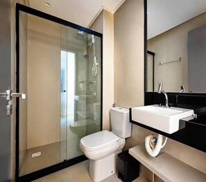 Une salle de bain moderne avec une douche à parois de verre, des toilettes blanches et un plan de toilette noir sur lequel est posé un lavabo blanc.
