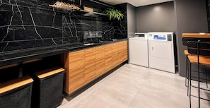 A modern kitchen with a black marble countertop, wooden cabinets, and a built-in washing machine. - Breeze Residence (João Pessoa)
