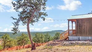 Eine rustikale Holzhütte mit Veranda, eingebettet in eine felsige Landschaft und von Bäumen umgeben.