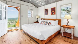 Un dormitorio con cama de madera, ropa de cama blanca, ventilador de techo y vistas al exterior.