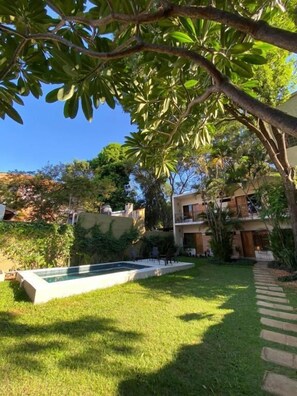 A pool with a stone border, surrounded by a well-maintained lawn and a tree. - De la Mora Hostal (Fernando De La Mora)