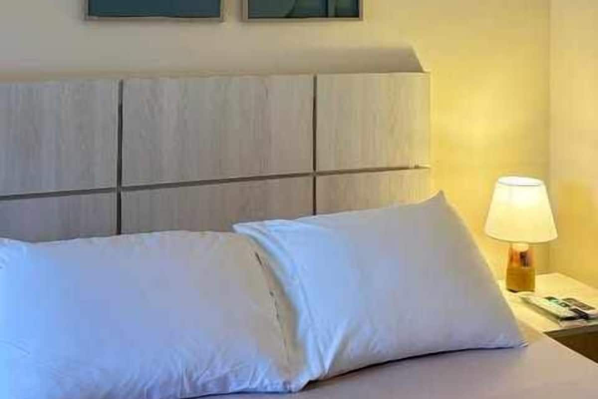 A bed with white bedding, a wooden headboard, and two abstract wall art pieces.