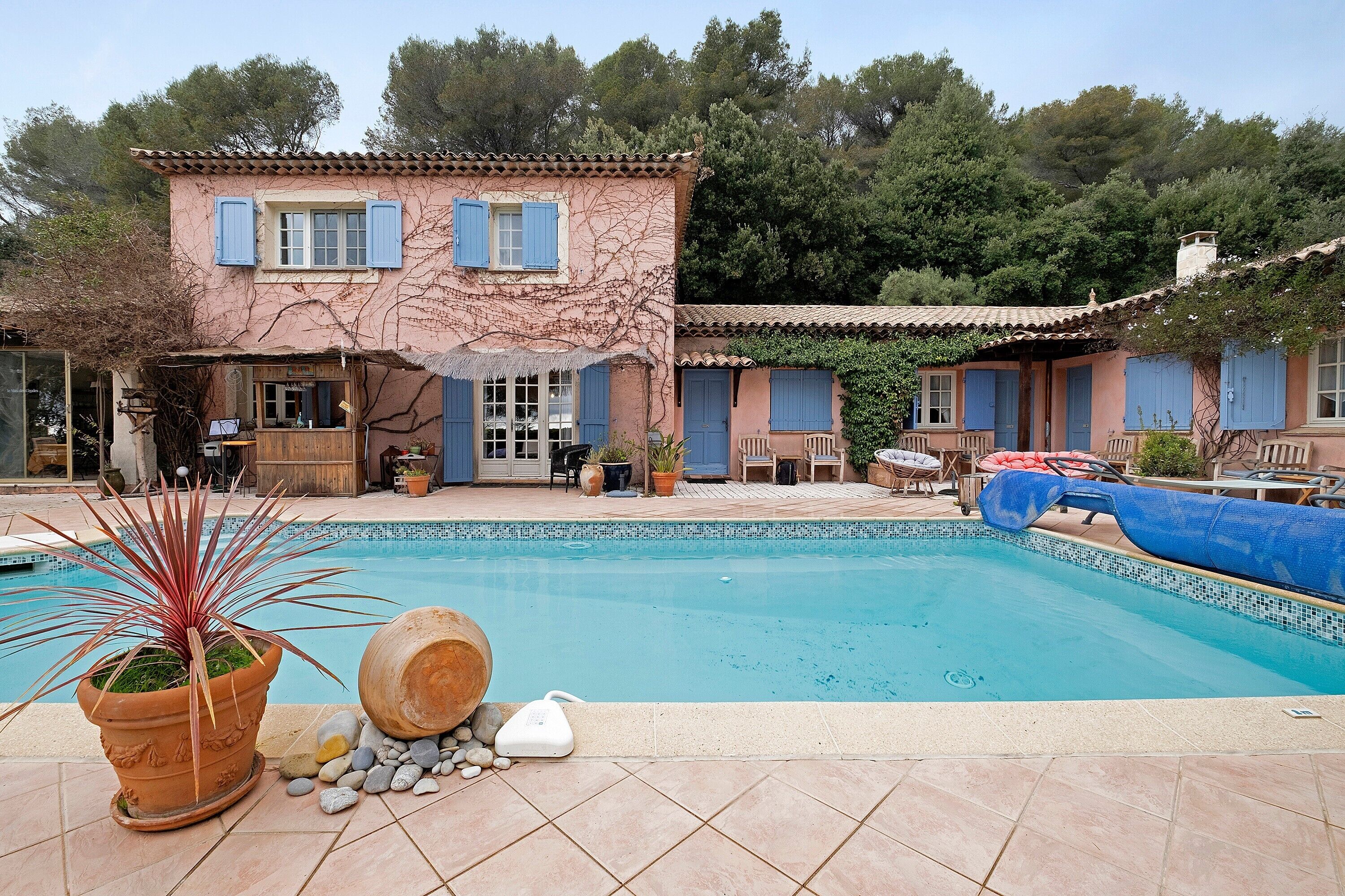 A pool area with a house, a potted plant, and a water heater.