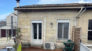A stone building with a tiled roof, a wooden deck, and a small table with chairs. - Duplex Cosy à Floirac - Your Haven of Light and Comfort (floirac)