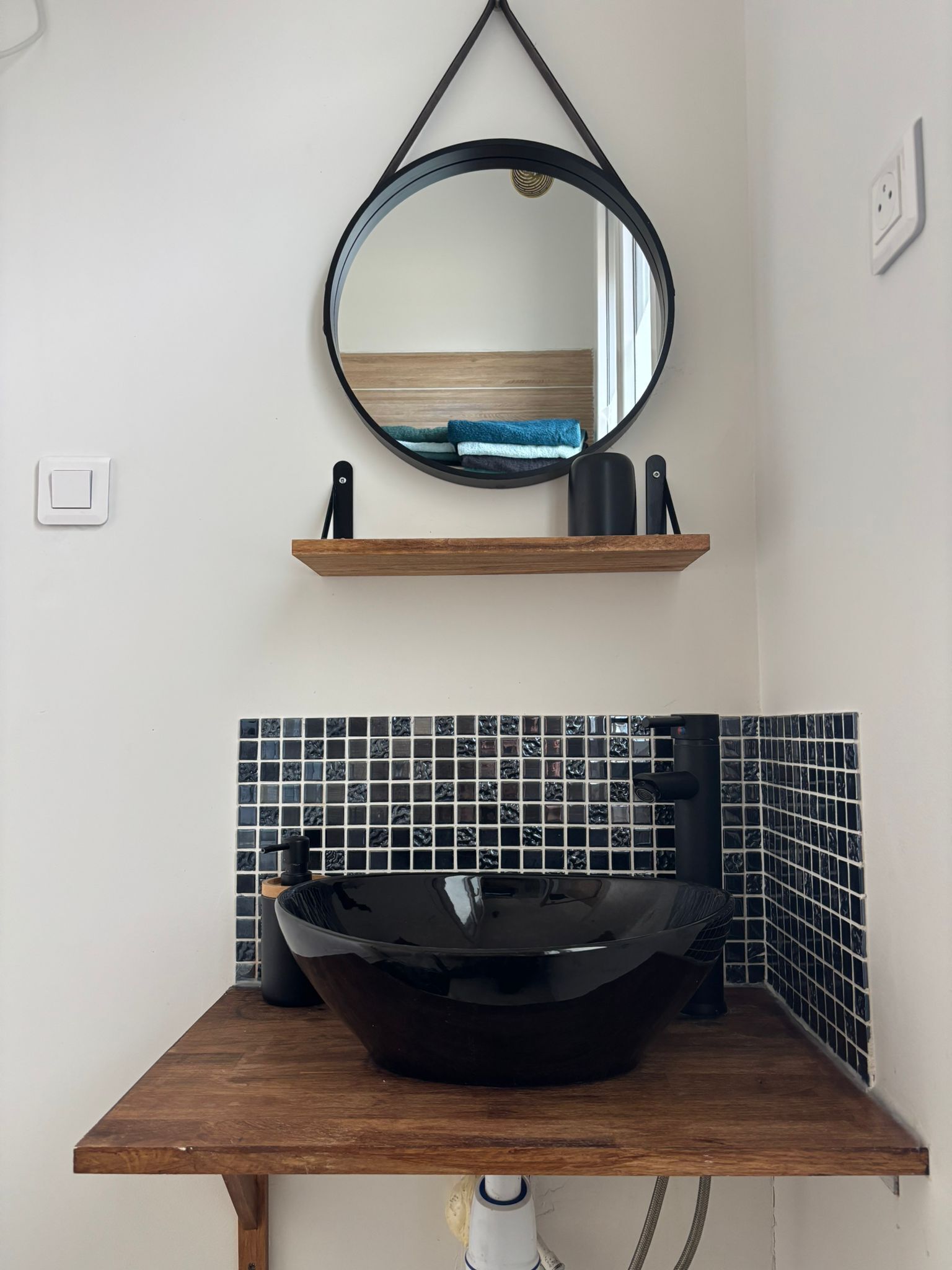 A bathroom with a wooden vanity, a black vessel sink, and a round mirror above.