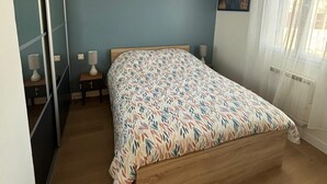 A bedroom with a bed, a nightstand, a lamp, and a window with curtains. - Duplex Cosy à Floirac - Your Haven of Light and Comfort (floirac)