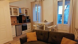 A compact living space with a kitchenette, a sofa with cushions, and a dining area. - Duplex Cosy à Floirac - Your Haven of Light and Comfort (floirac)
