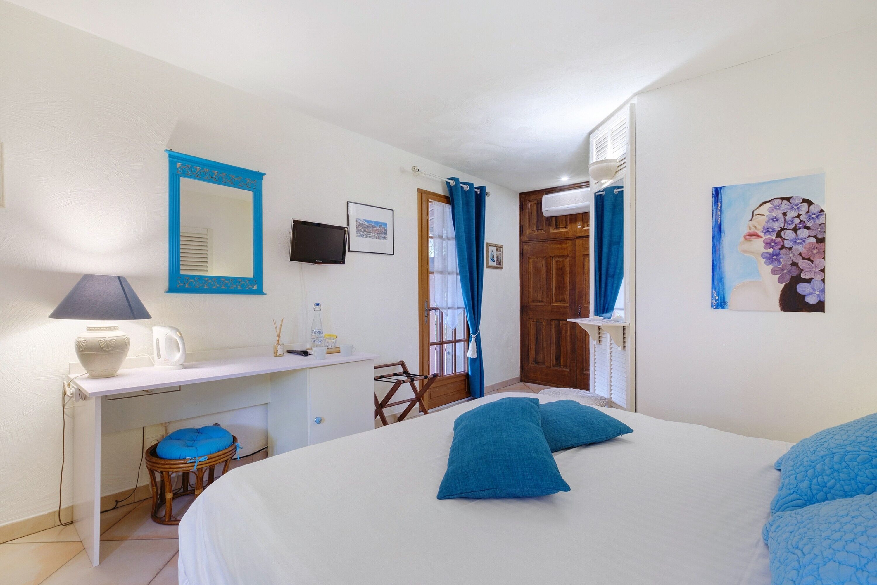 Quarto com cama, escrivaninha, cadeira, televisão e porta.