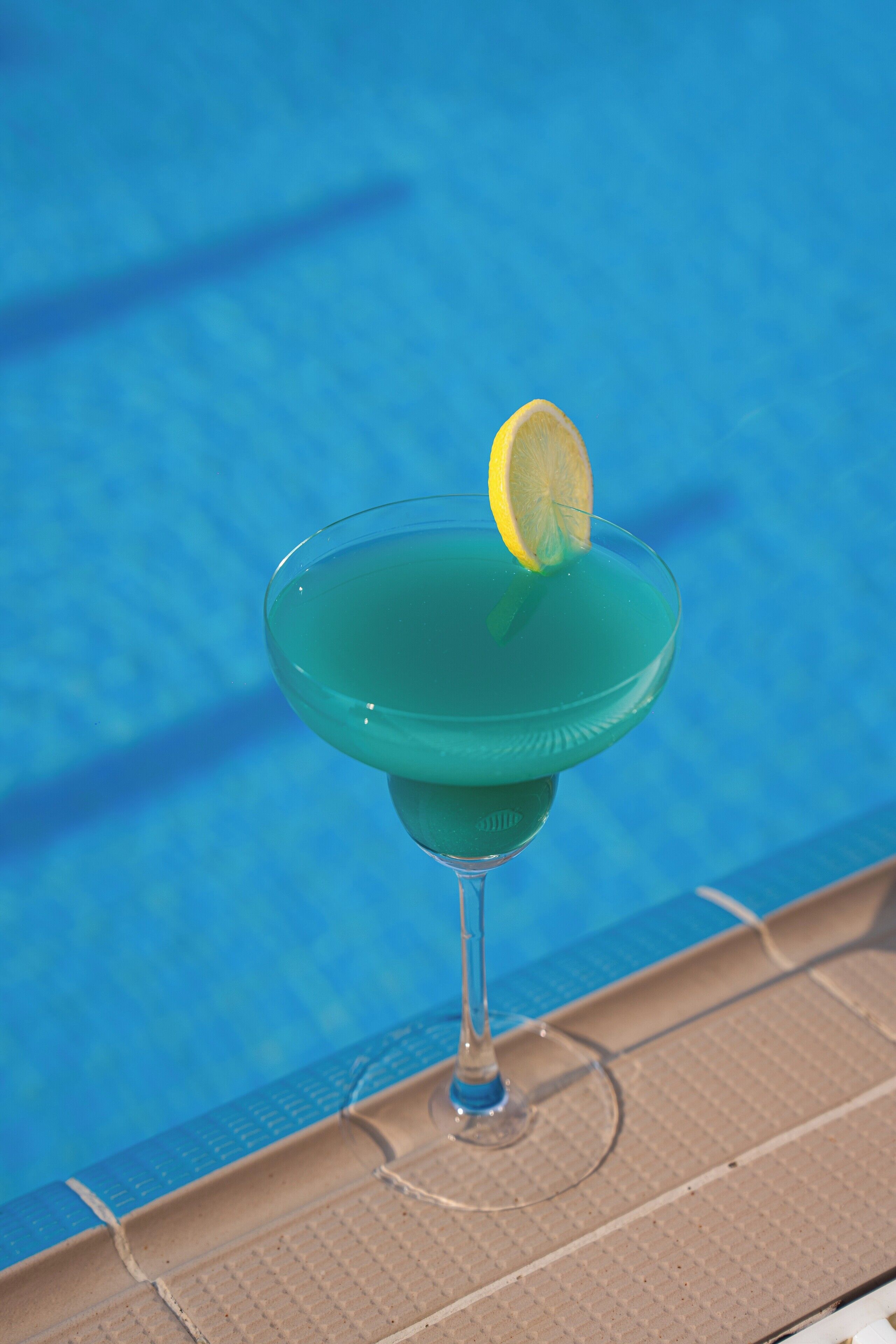 A cocktail glass with a lemon garnish on a poolside bar.
