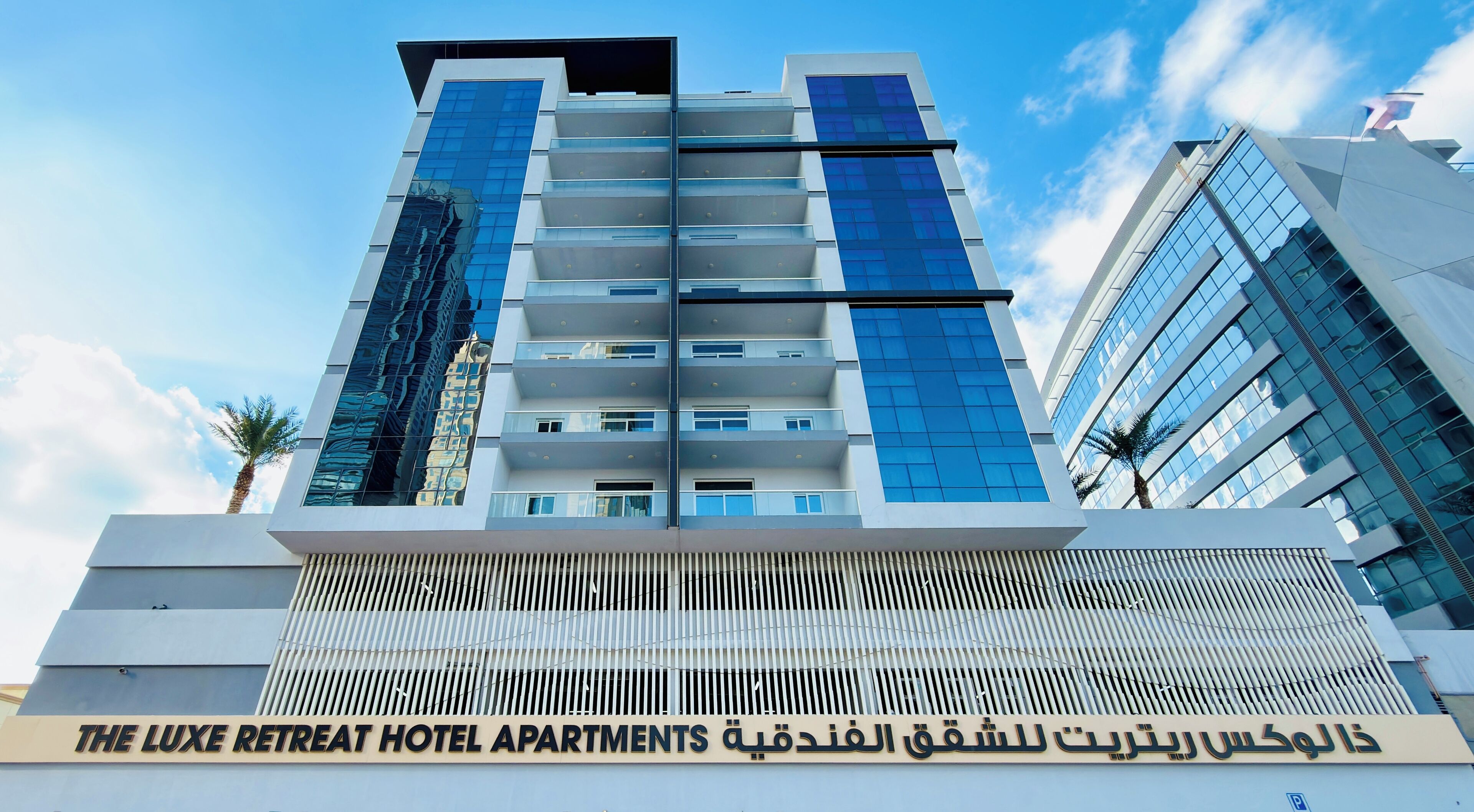 A modern hotel building with a sign indicating "The Luxe Retreat Hotel Apartments".