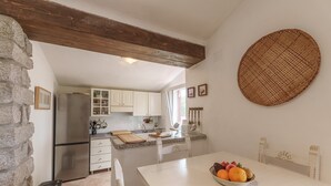 A kitchen with white cabinets, a stainless steel refrigerator, a wooden ceiling beam, and a fruit bowl on the island.