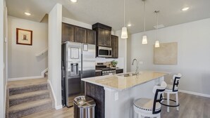Una cocina moderna con armarios oscuros, electrodomésticos de acero inoxidable, una isla con encimera de granito y dos taburetes de bar.