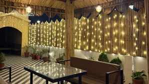 An indoor patio area with a bamboo ceiling, string lights, and a checkered floor. - SM Hotel (Ghaziabad)