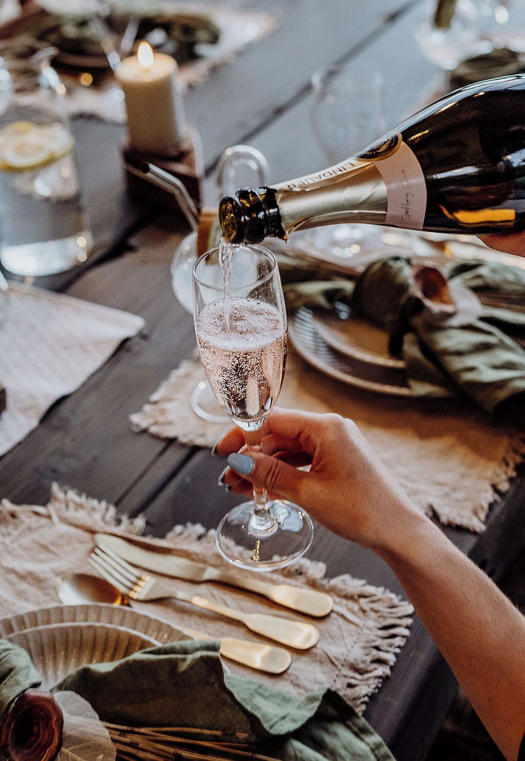 A hand holding a champagne flute filled with bubbles, with a bottle being poured into it.