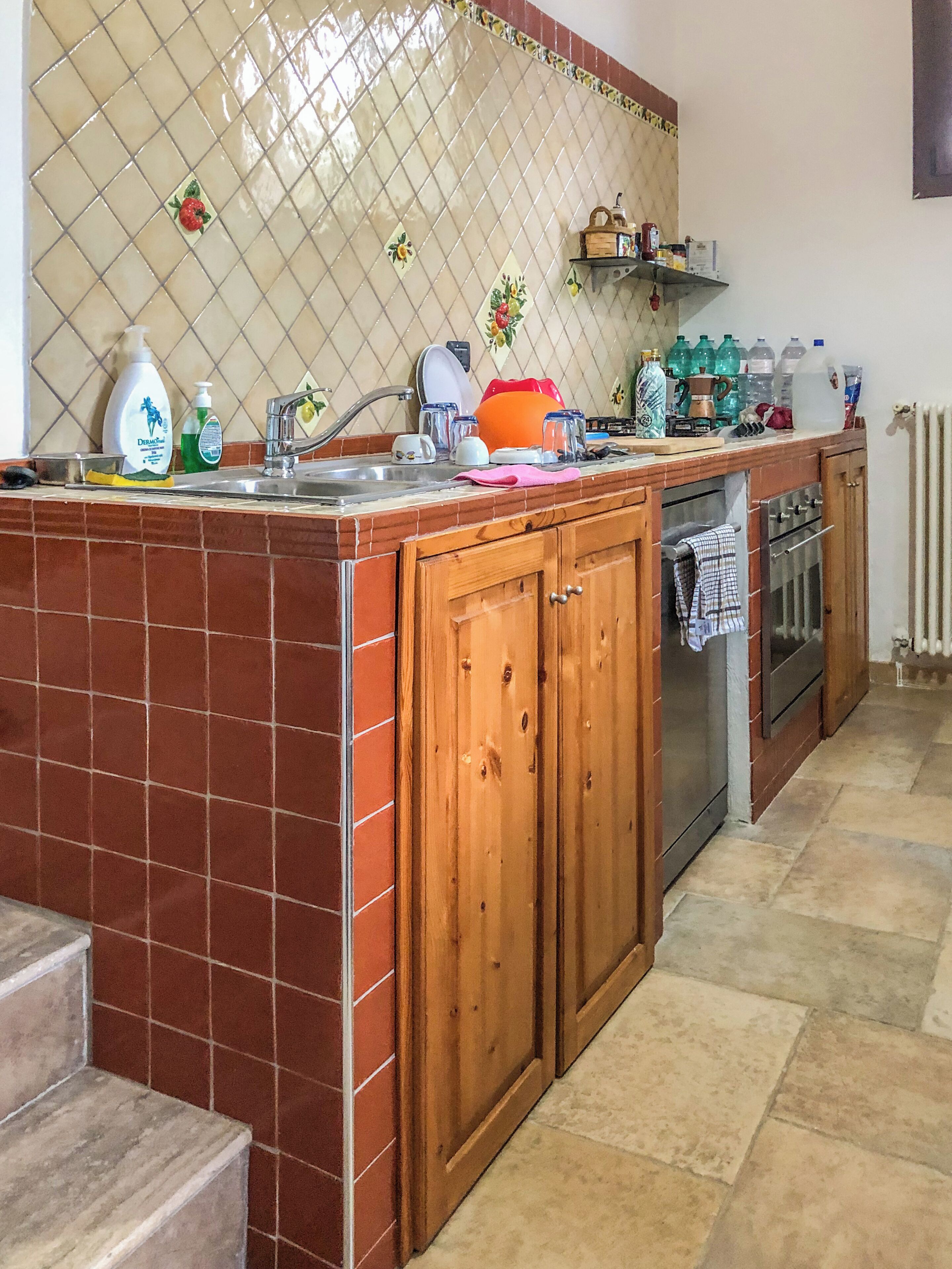 A kitchen with a tiled backsplash, wooden cabinets, a sink, and various kitchen items.