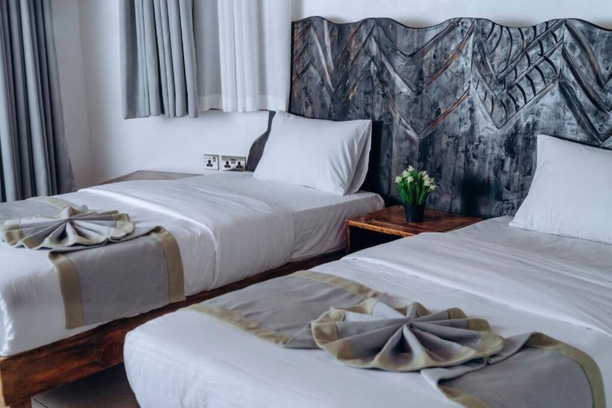 A hotel room with two beds, a wooden headboard, and a nightstand with a vase of flowers.