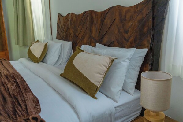 Una cama bien hecha con sábanas blancas y dos almohadas, una marrón y otra beige, en una habitación con cabecera de madera y una lámpara de noche.