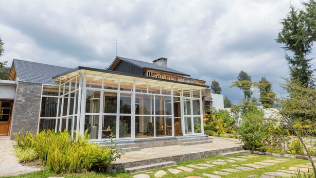 Uma casa moderna com varanda envidraçada, degraus de pedra e um jardim com diversas plantas.