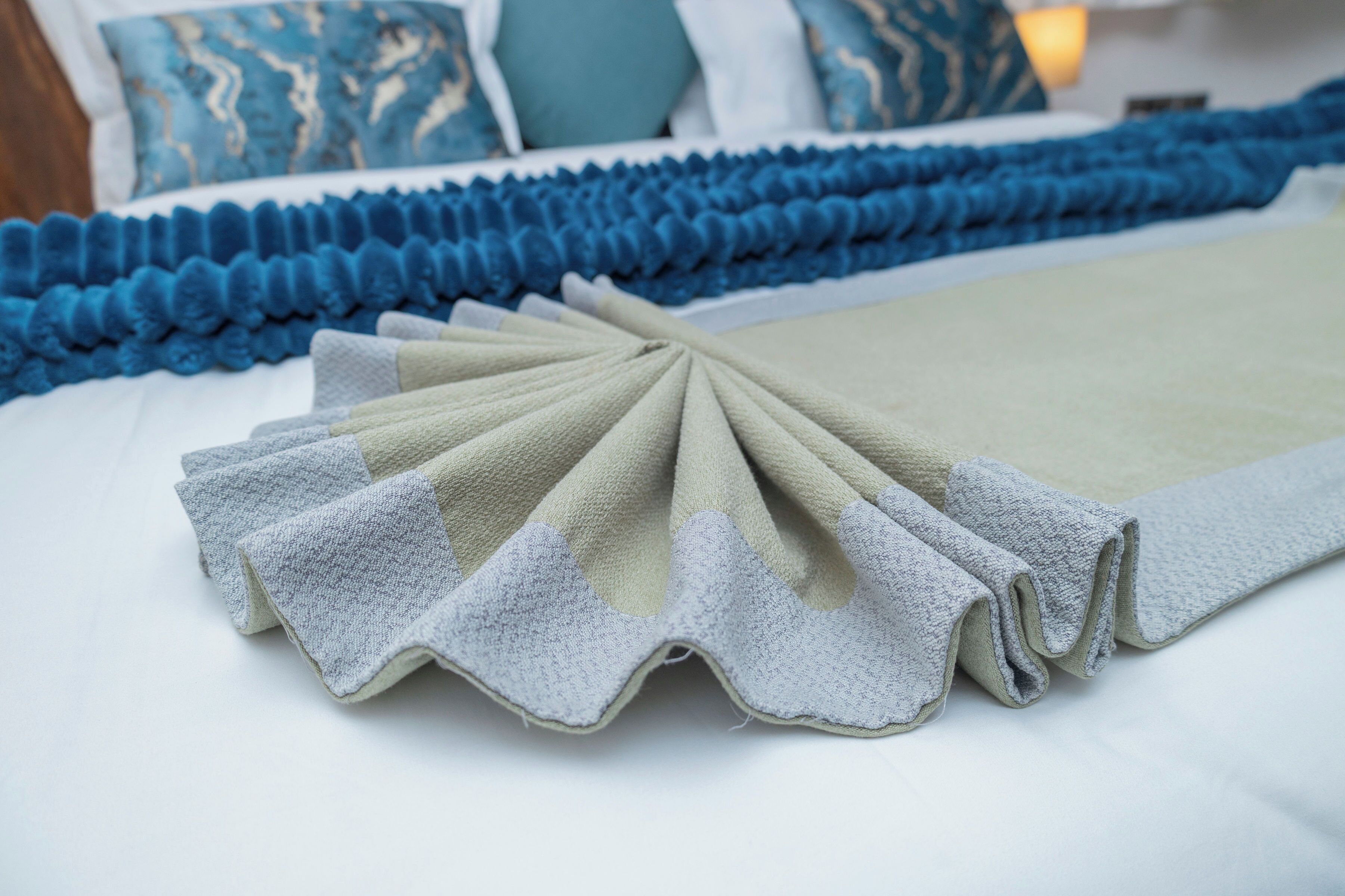 A neatly made bed with a blue and beige bedspread, a blue decorative bed skirt, and a blue and beige pillow arrangement.