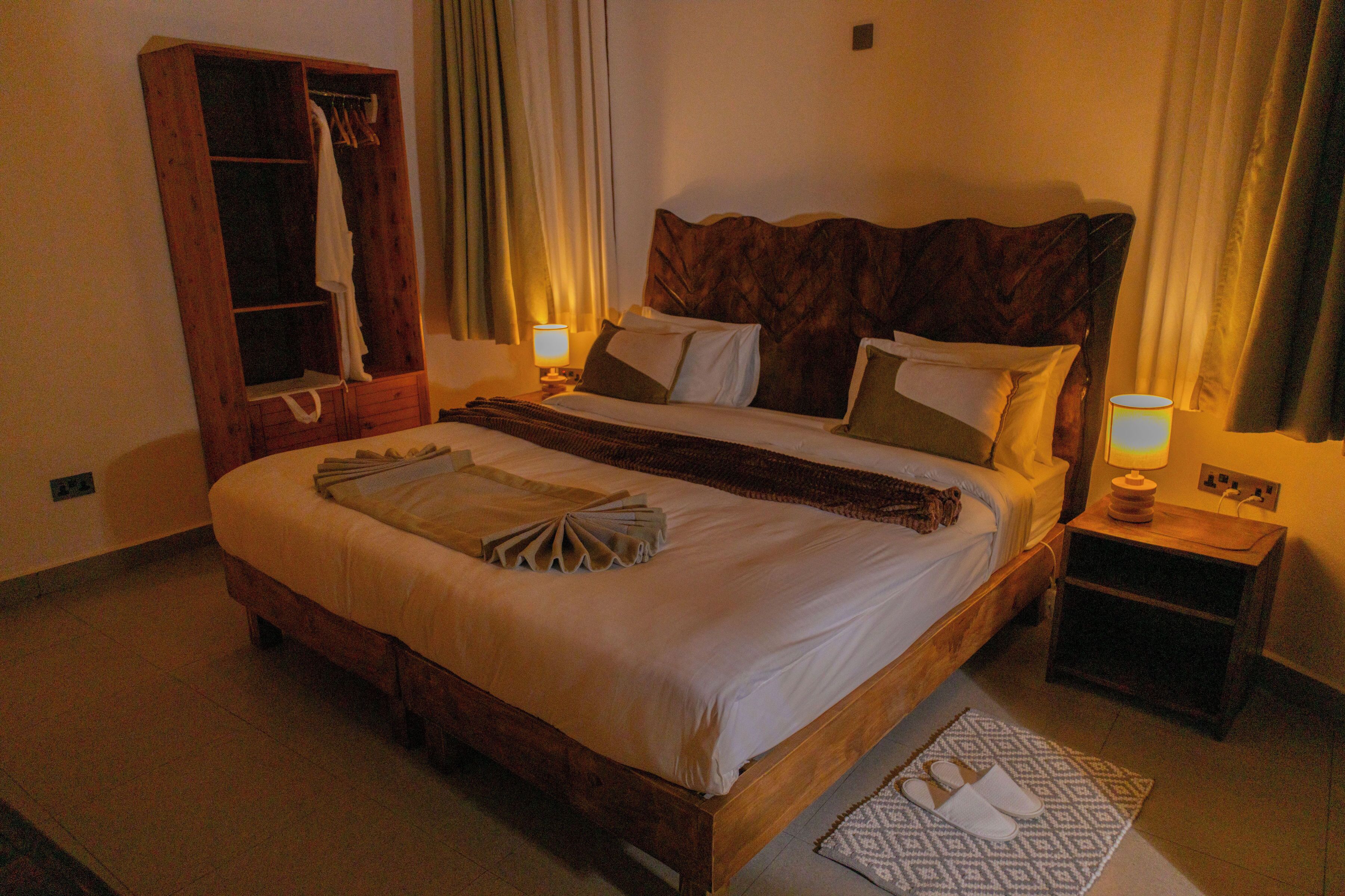 Ein Hotelzimmer mit einem großen Bett, einem Holzschrank, einem Nachttisch mit Lampe und einem gemusterten Teppich.
