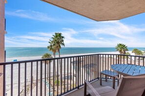 Un balcone con vista sulla spiaggia, palme e cielo sereno.