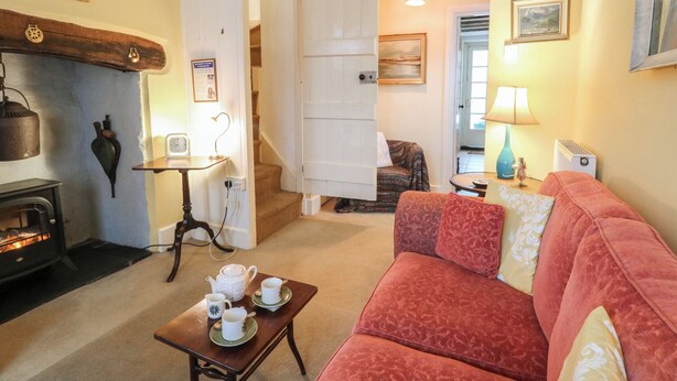 A cozy living room with a fireplace, a sofa, a table with teacups, and a staircase leading to another room. - 6 Church Lane (Llanidloes)