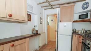 A compact kitchen with wooden cabinets, a white refrigerator, a microwave, and a toaster. - 6 Church Lane (Llanidloes)