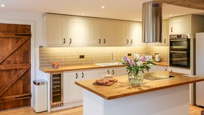 A modern kitchen with white cabinets, a wooden countertop, a stainless steel range hood, and a built-in oven. - Lake View (Crediton)