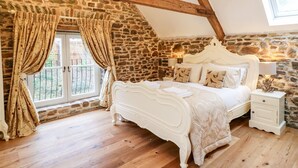 A bedroom with a stone wall, wooden beams, a white bed, and a window with curtains. - Lake View (Crediton)