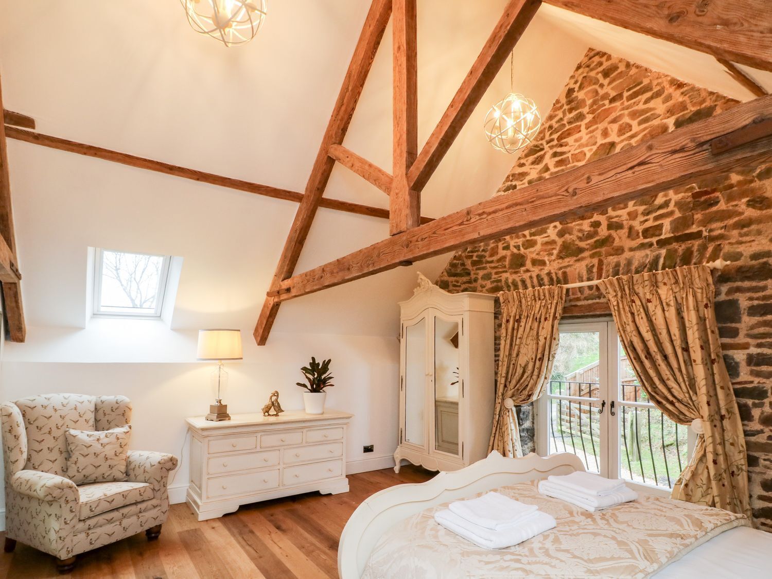 Un dormitorio espacioso con una cama grande, techo de madera, pared de piedra y una ventana con cortinas.