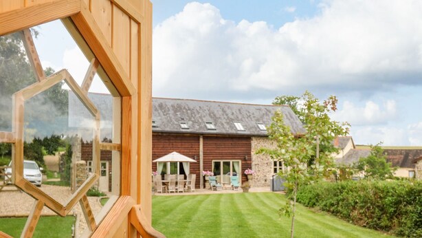 A wooden structure with a large window, a well-maintained lawn, and a building with a sloped roof in the background. - Lake View (Crediton)