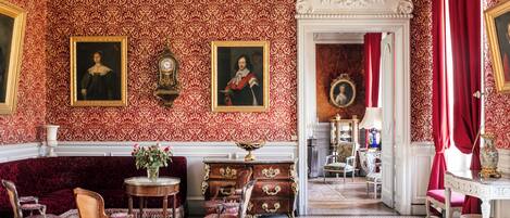 Um quarto com papel de parede estampado, um candelabro, um sofá, cadeiras, uma mesa e um aparador.