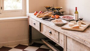Une cuisine avec des ustensiles de cuisine en cuivre accrochés au mur, un plan de travail en bois sur lequel repose une bouteille de vin, et un sol à carreaux.