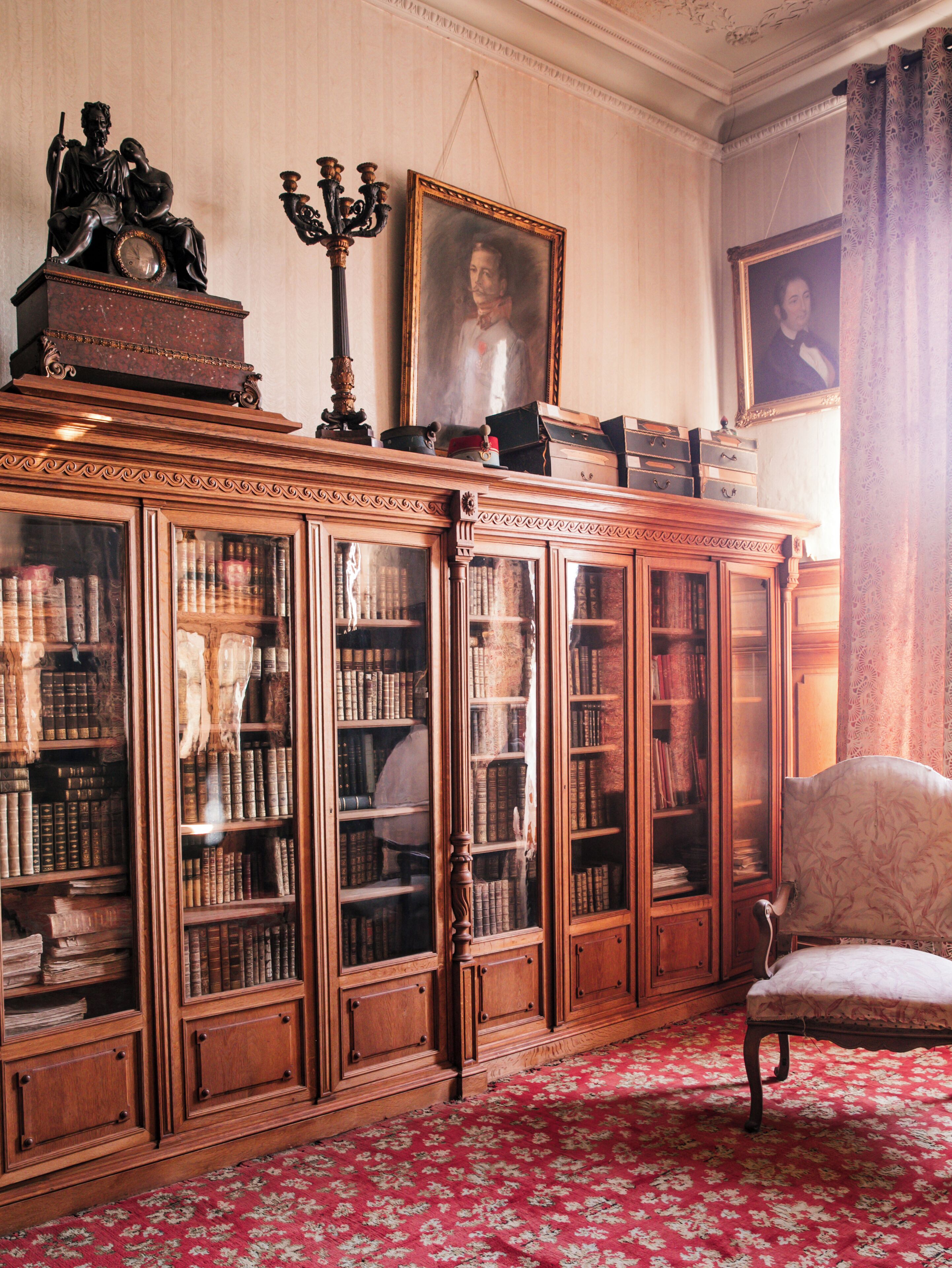 A room with a large wooden bookcase filled with books, a red patterned carpet, and a chair.