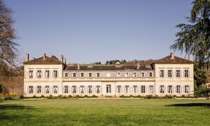 A large, symmetrical building with a central entrance, flanked by two wings, set in a spacious, well-maintained lawn.