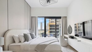 A modern bedroom with a large bed, a TV, and a balcony with city views. - Chic Modern Studio in Meydan (Dubai)