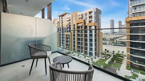 A balcony with two wicker chairs and a small table, overlooking a modern apartment building with multiple floors and balconies. - Chic Modern Studio in Meydan (Dubai)