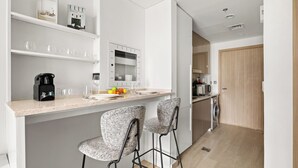 A modern kitchen with a marble countertop, two bar stools, a coffee machine, and a microwave. - Chic Modern Studio in Meydan (Dubai)