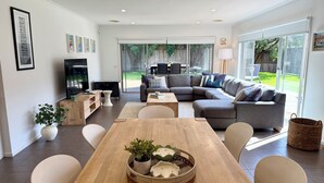 En moderne stue med et træspisebord, en grå hjørnesofa, et fladskærms-tv og en stor skydedør til en baghave.