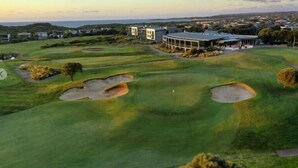 En golfbane med bunkers, et klubhus og udsigt over det omkringliggende landskab.